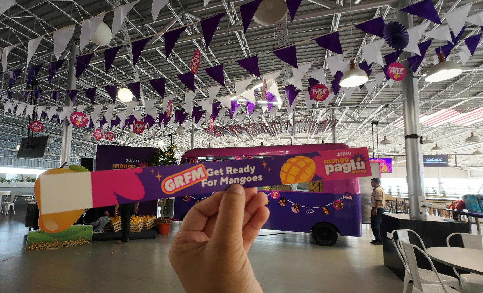 A GRFM - get ready for mangoes - paper wristband held up in front of the truck, the bunting and carbide-free roundels running across the ceiling behind it